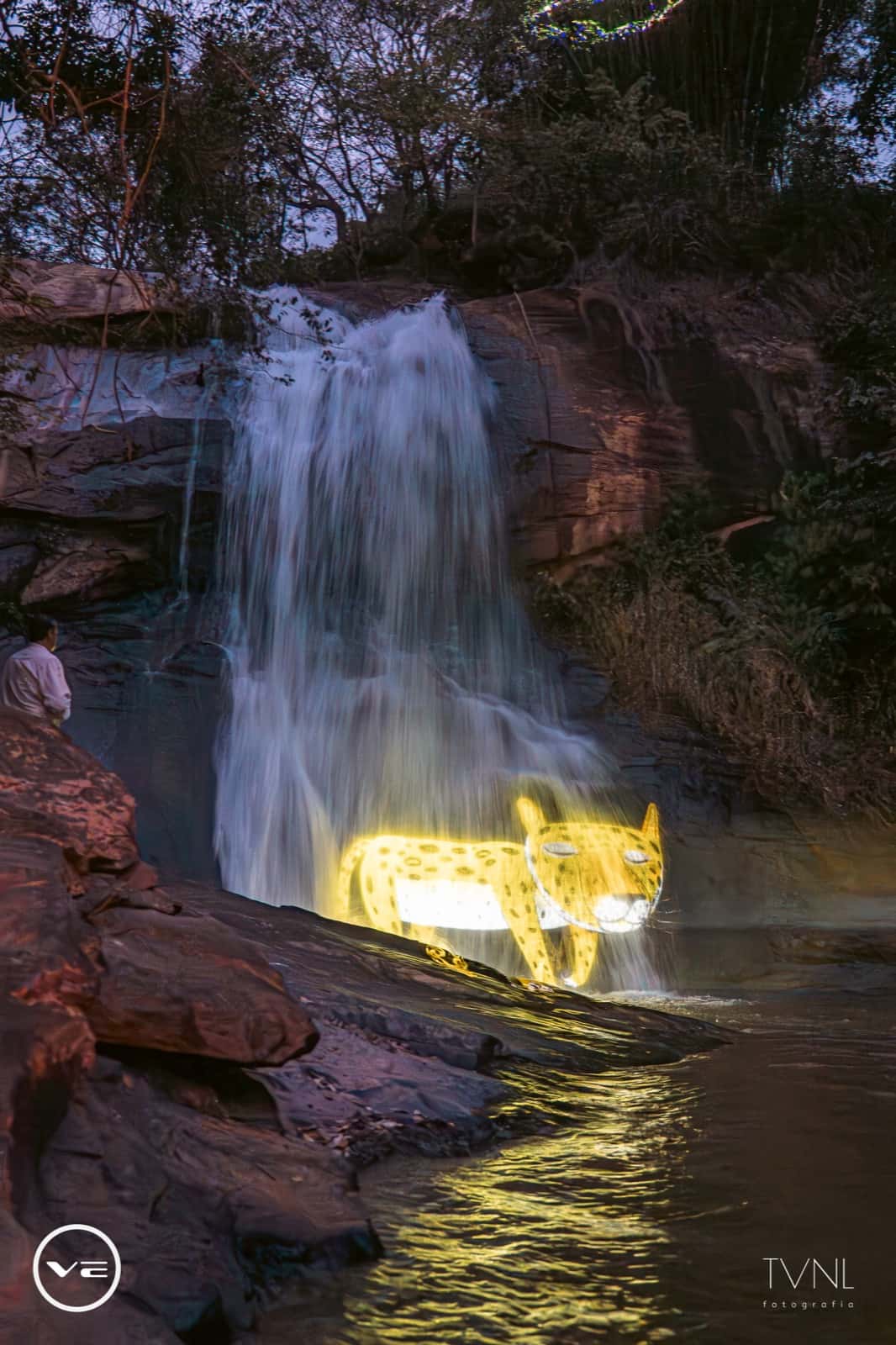 Cachoeira ao entardecer com uma onça desenhada em luz