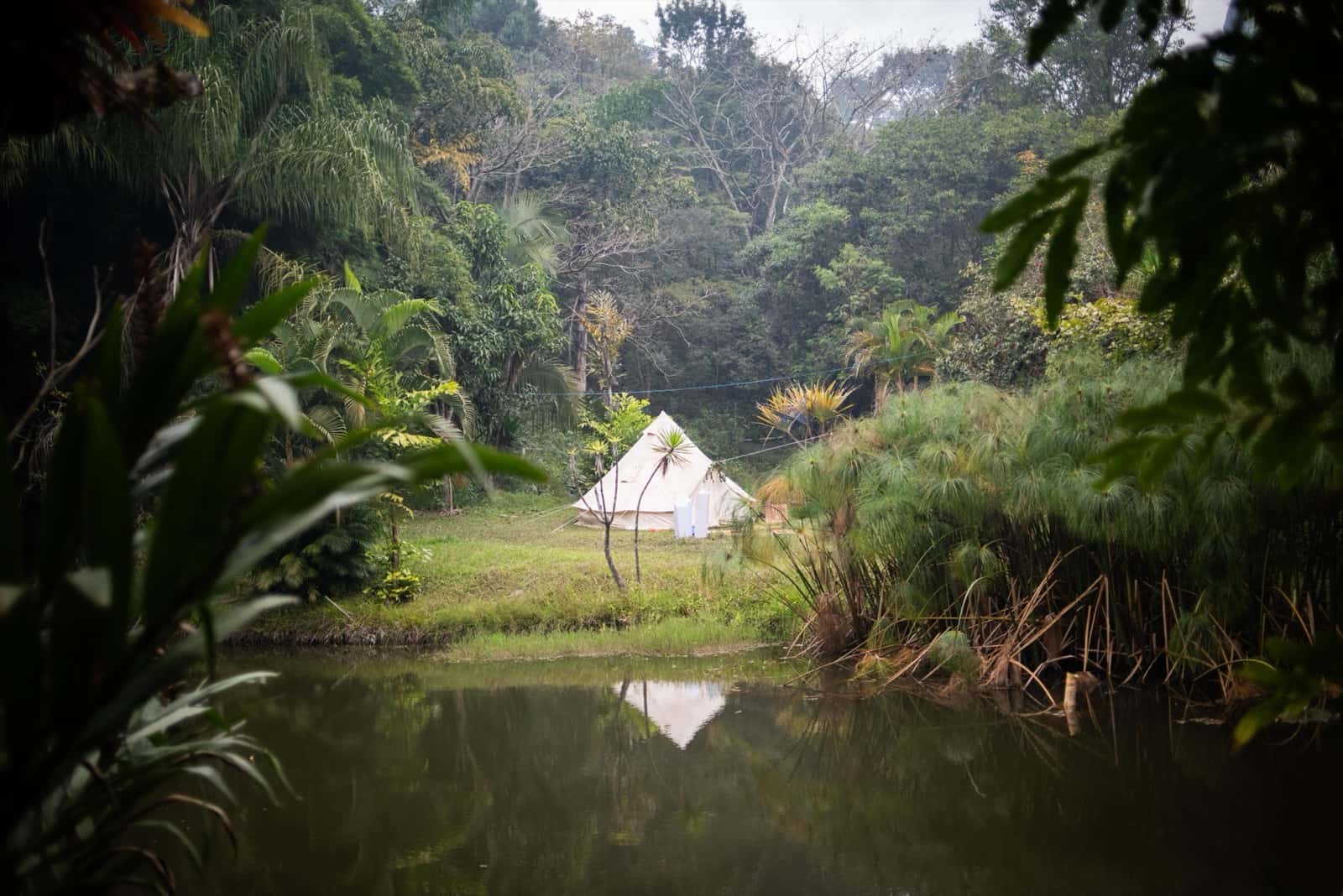 Barraca branca refletida no lago, mata ao redor