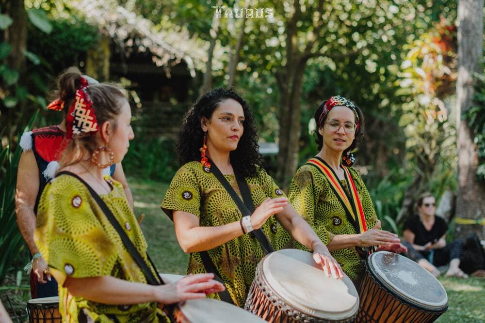 Trio percutindo djembês em vestidos estampados
